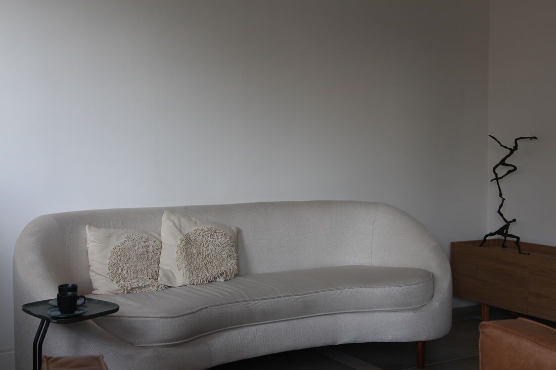 Sofá claro do consultório, com uma xícara preta na mesa lateral e uma escultura de ferro ao fundo